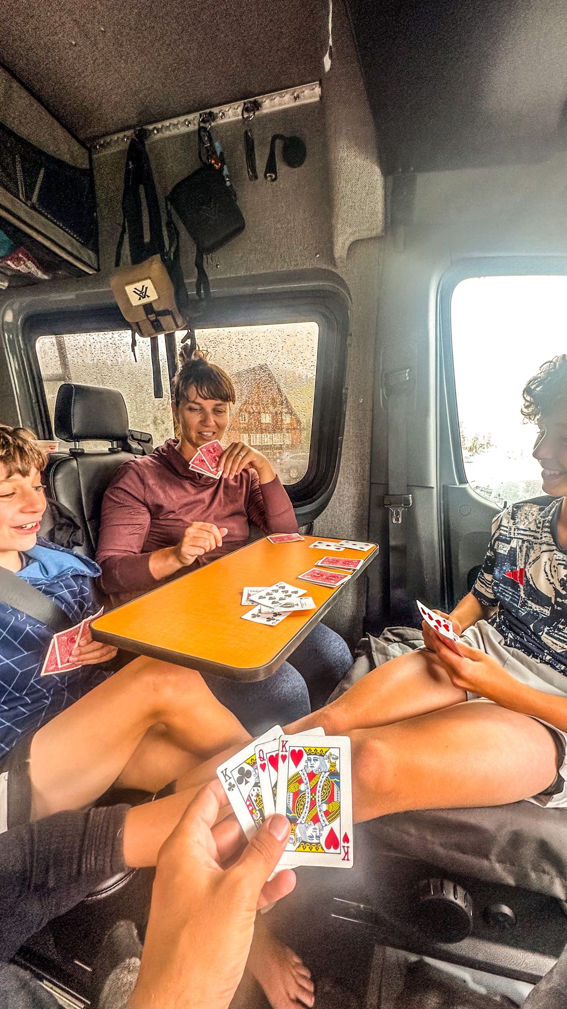 Inside a cozy RV rental, a family laughs while playing cards, making the most of a rainy travel day.