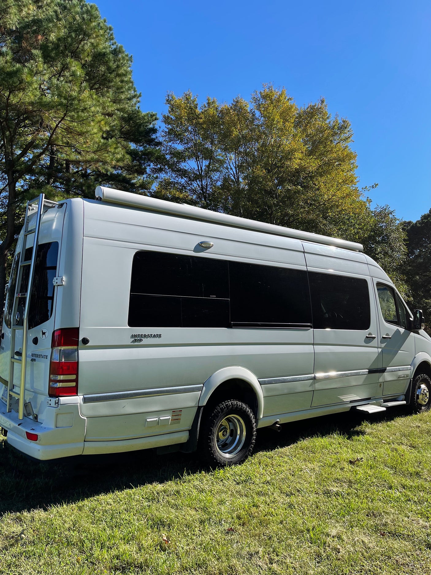 White Airstream Interstate 4WD RV rental, a luxury camper van, parked on green grass with blue sky above.