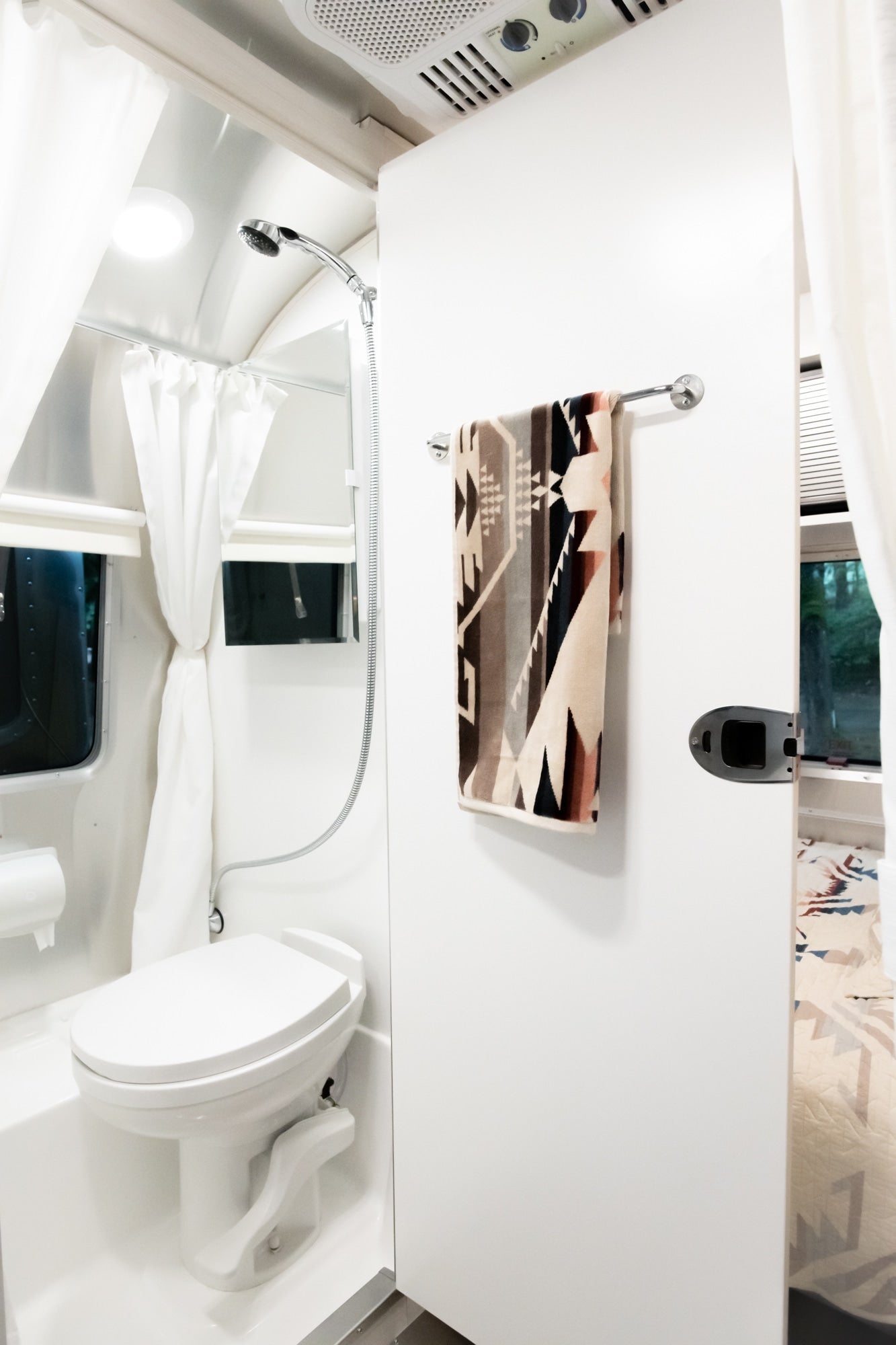 This RV rental features a bright, compact bathroom with a toilet, shower, and tribal-patterned towel.