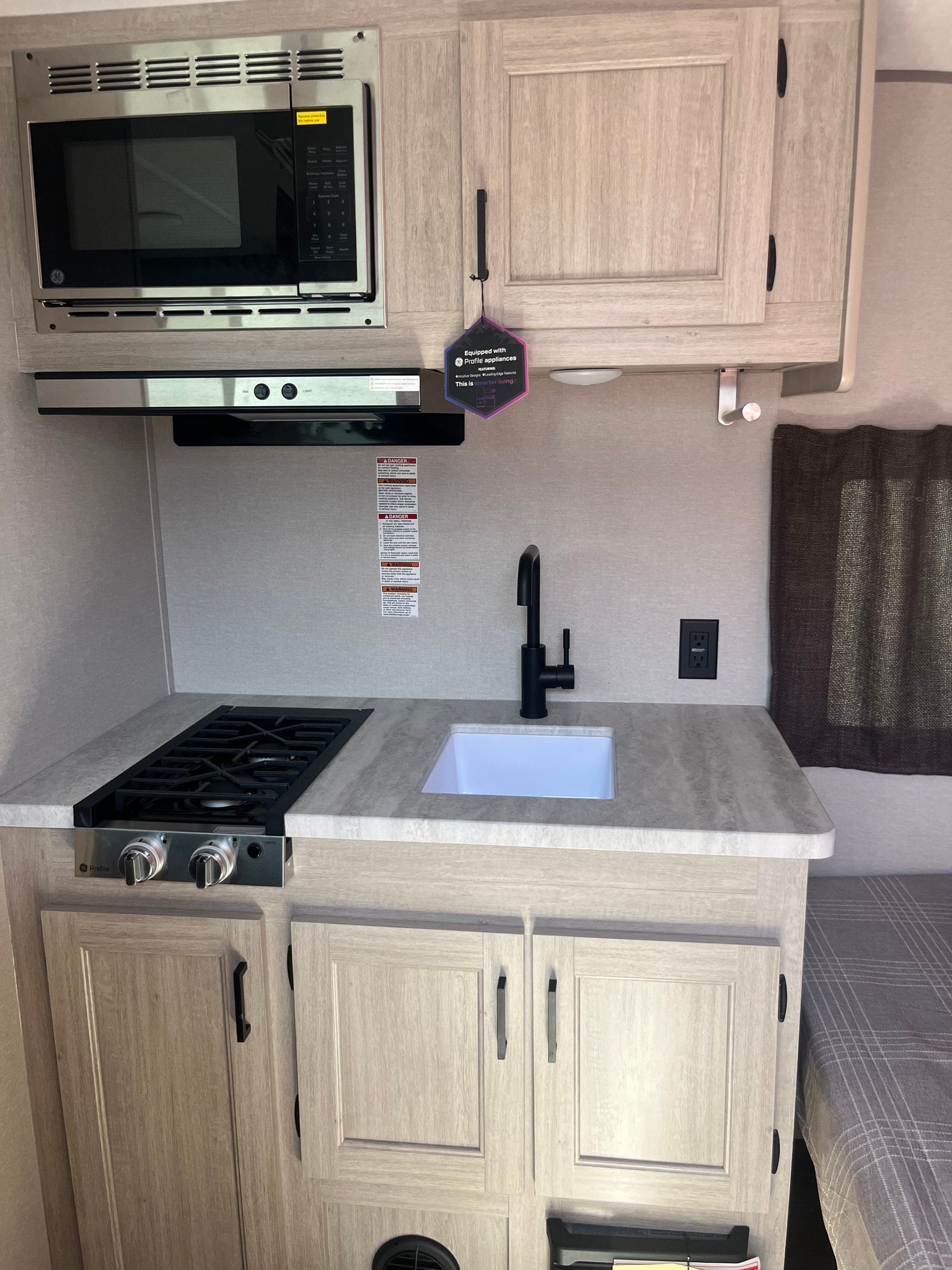 Modern rv rental kitchen featuring a GE Profile microwave, compact gas stove, and sink, designed for efficient travel living.