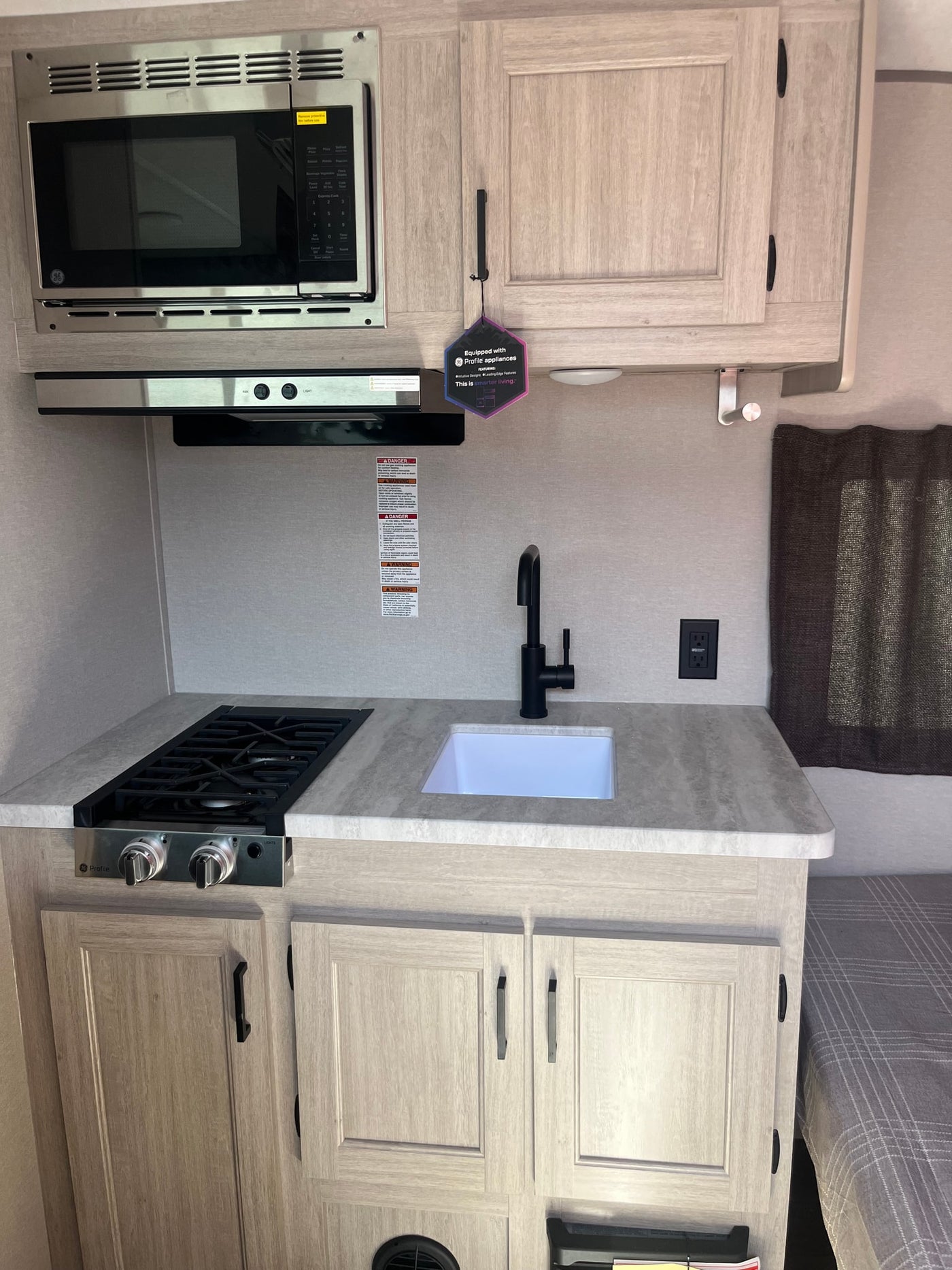 Modern rv rental kitchen featuring a GE Profile microwave, compact gas stove, and sink, designed for efficient travel living. — photo 4