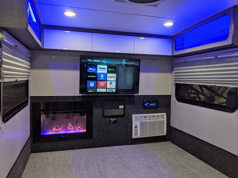 This modern rv rental interior features a TCL Roku TV, electric fireplace, AC unit, and ambient blue lighting for comfortable travel.