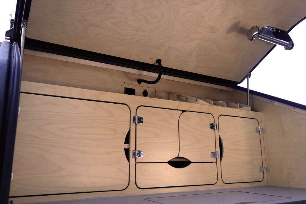 alongside an interior white frame and wooden wall.|Inside an RV rental: a textured purple cushion forming a bed or seat