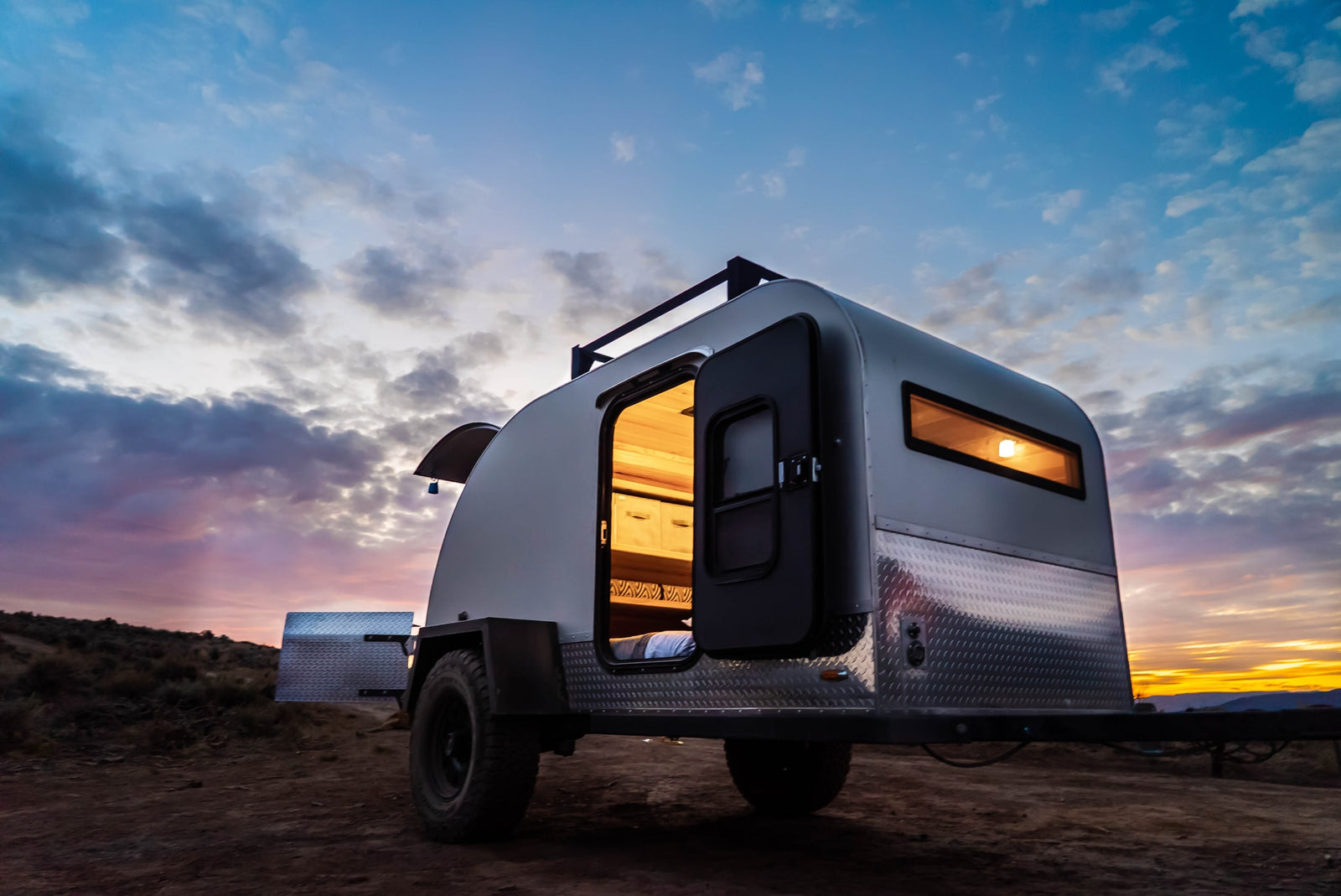 Cozy teardrop trailer rv rental illuminated at sunset, ready for camping in the desert. Perfect for outdoor travel.
