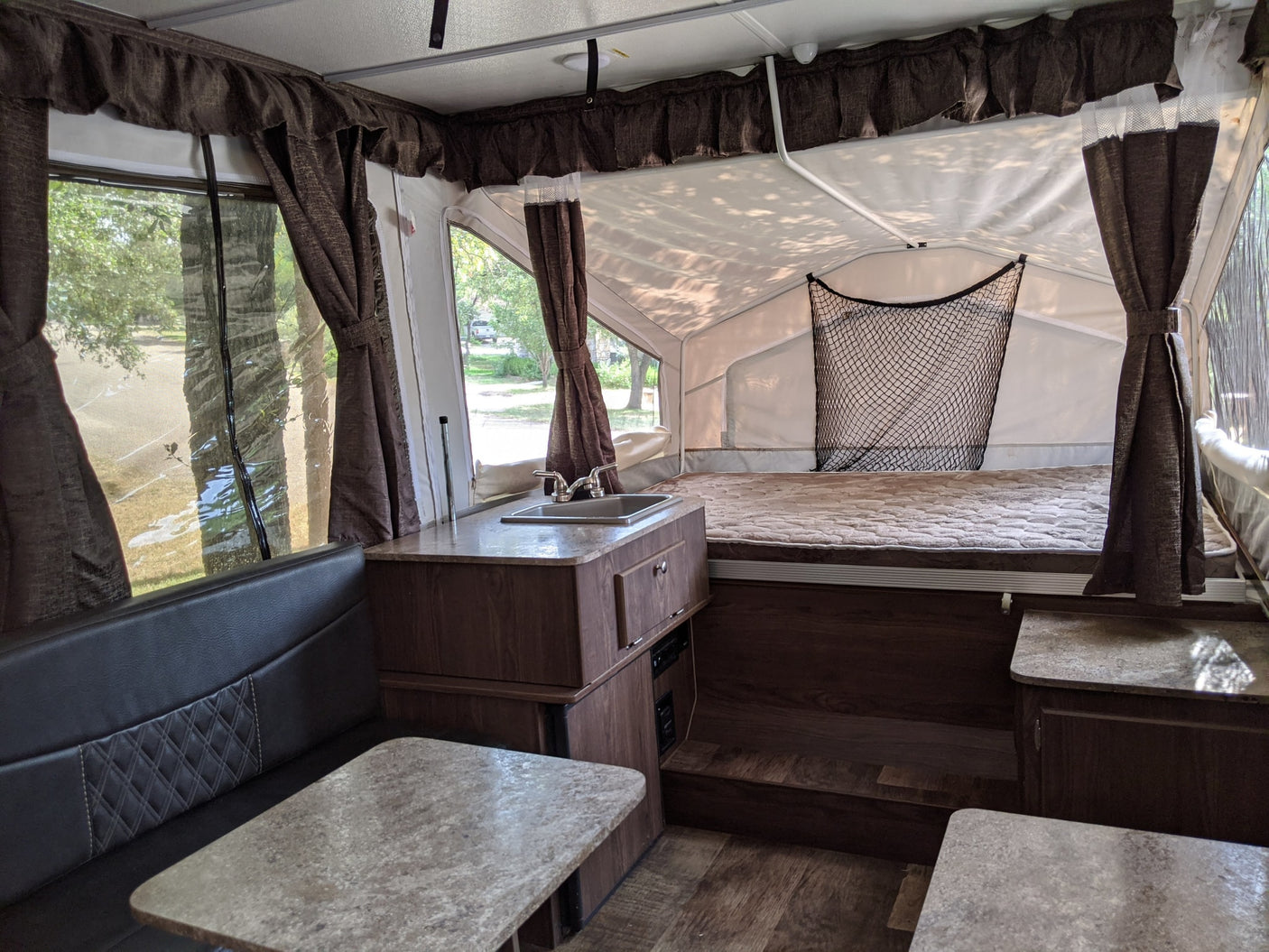 An inviting pop-up camper interior, ready for your next RV rental adventure. Features comfortable dinette, functional kitchen, and dual bed areas.