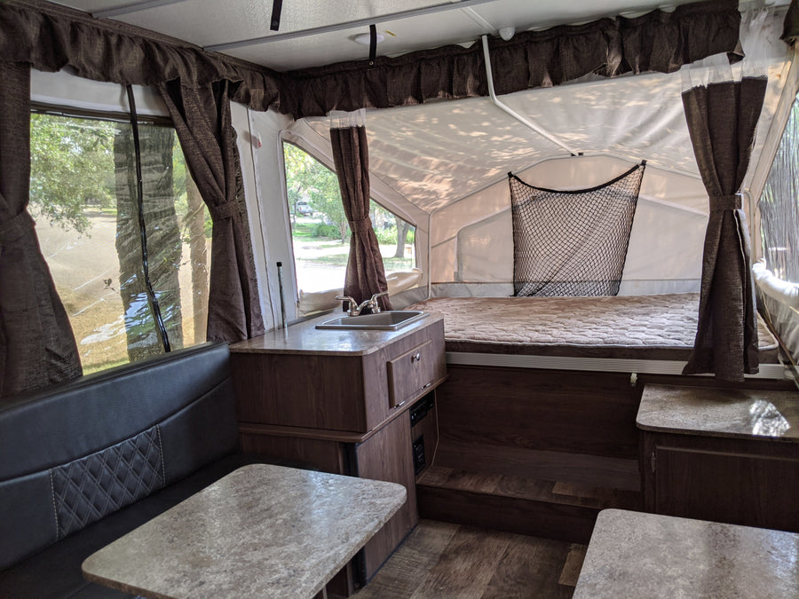 An inviting pop-up camper interior, ready for your next RV rental adventure. Features comfortable dinette, functional kitchen, and dual bed areas.