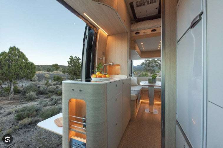 Explore nature in this stylish rv rental. Bright camper van interior features a modern kitchenette, dining, and scenic outdoor view.