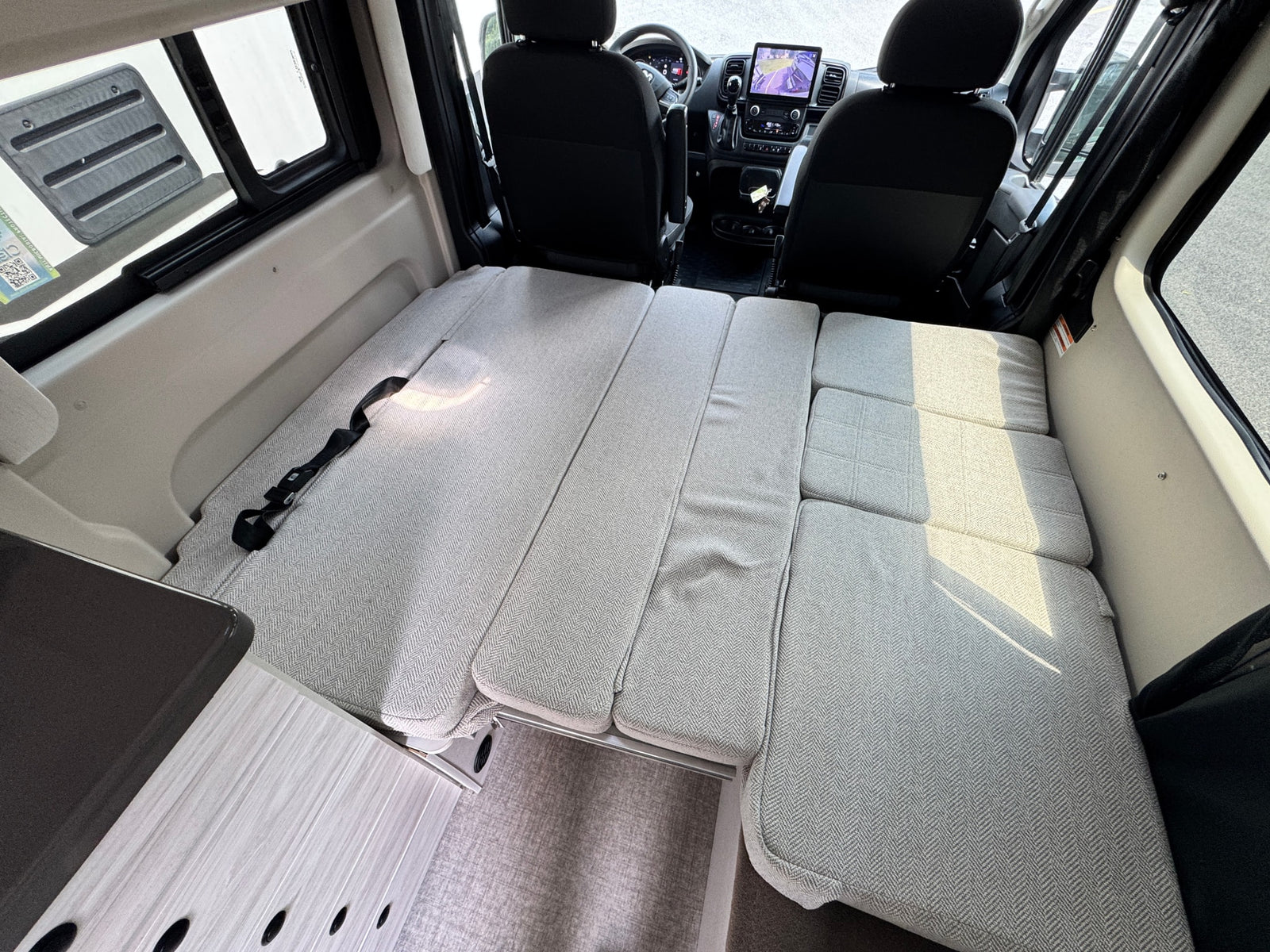 This rv rental features a convertible light grey cushion bed system. View from rear, showing cockpit and interior amenities.