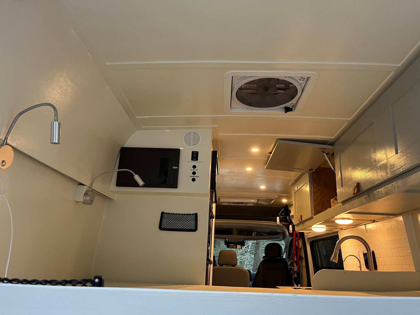 Bright RV rental interior with ceiling fan, control panel, reading lights, and kitchenette. View to front seats.