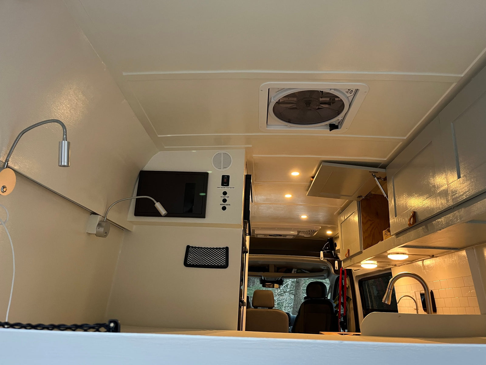 Bright RV rental interior with ceiling fan, control panel, reading lights, and kitchenette. View to front seats.