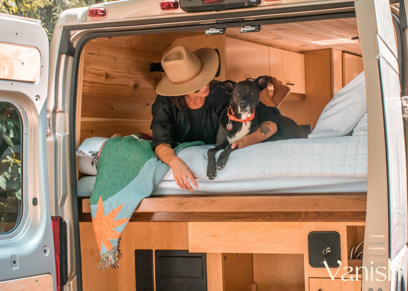 Inside a comfy RV rental: A person and dog relax on the bed of a wooden camper van. Ideal for travel life.