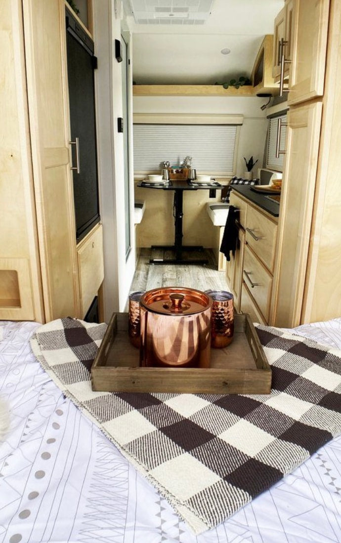Cozy RV rental interior with a modern kitchen, dinette, and a comfortable bed. Copper accents and checkered blanket add style.
