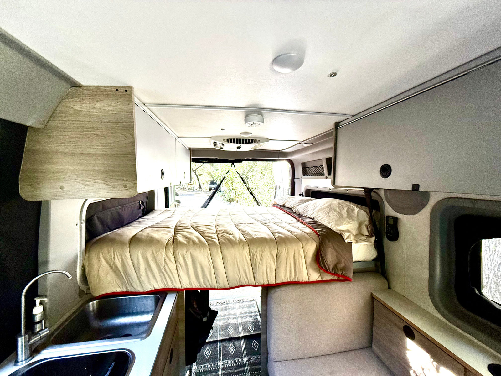Cozy rv rental interior featuring a comfortable bed, kitchenette, and overhead storage. Ideal camper van living space.