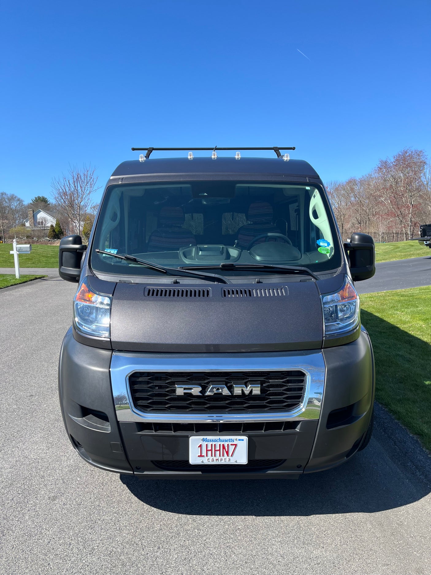 A gray Ram ProMaster camper van with roof rack lights, ideal for an rv rental road trip or vacation, parked on a clear day.