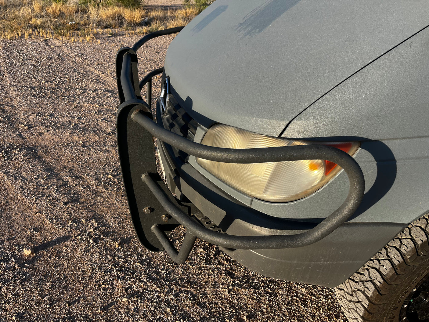 Adventure-ready gray RV rental with a black bull bar, off-road tire, and textured paint on a gravel path.