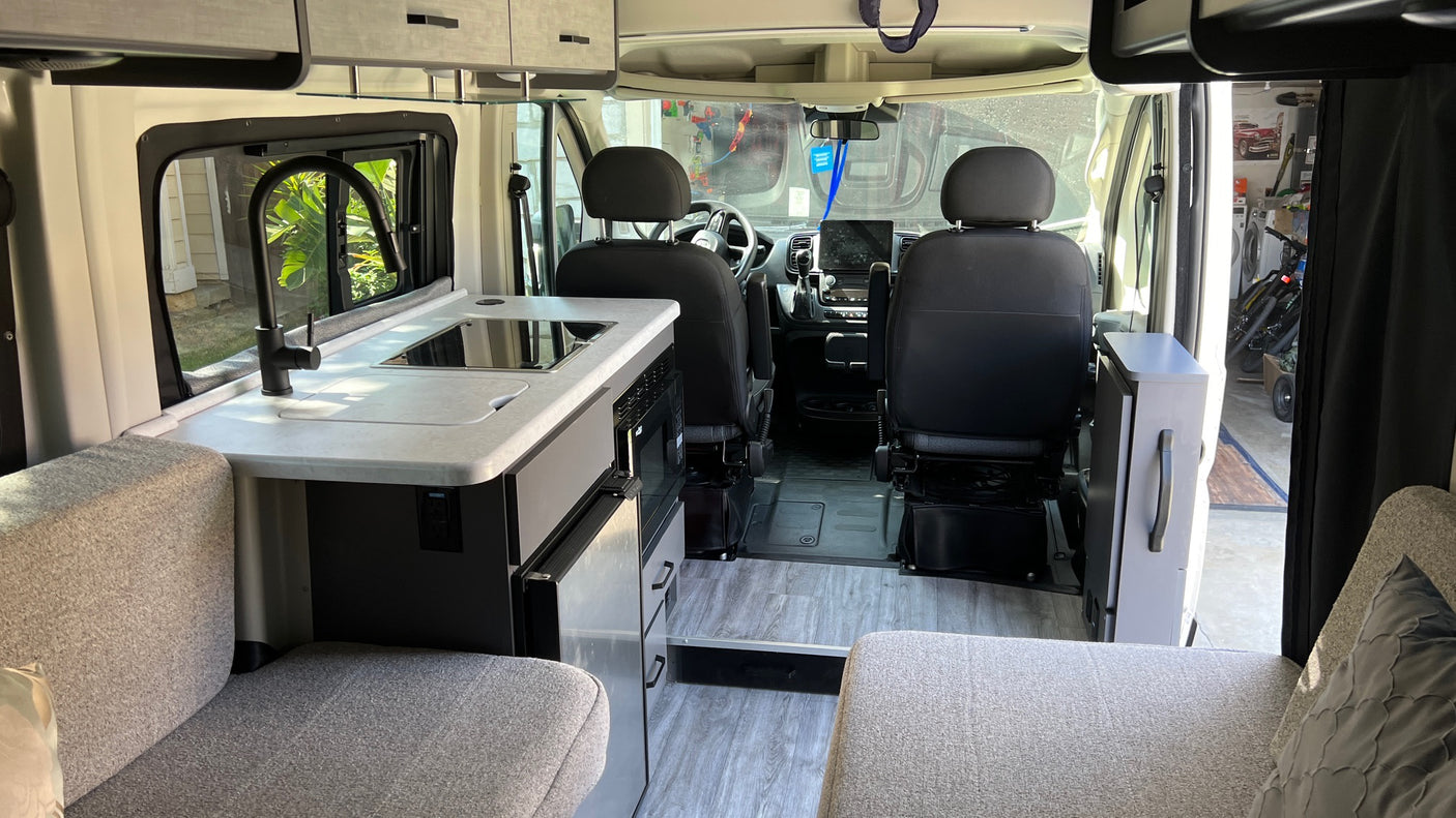 Modern RV rental interior, showing a kitchenette with sink/stove, seating areas, and cockpit view.