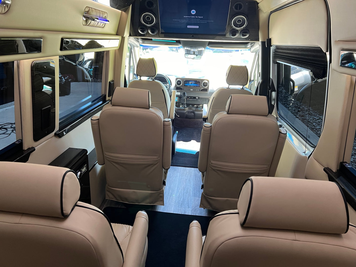 View inside a spacious RV rental, showcasing tan leather captain's chairs, a front TV, and wood-grain accents for luxury travel.