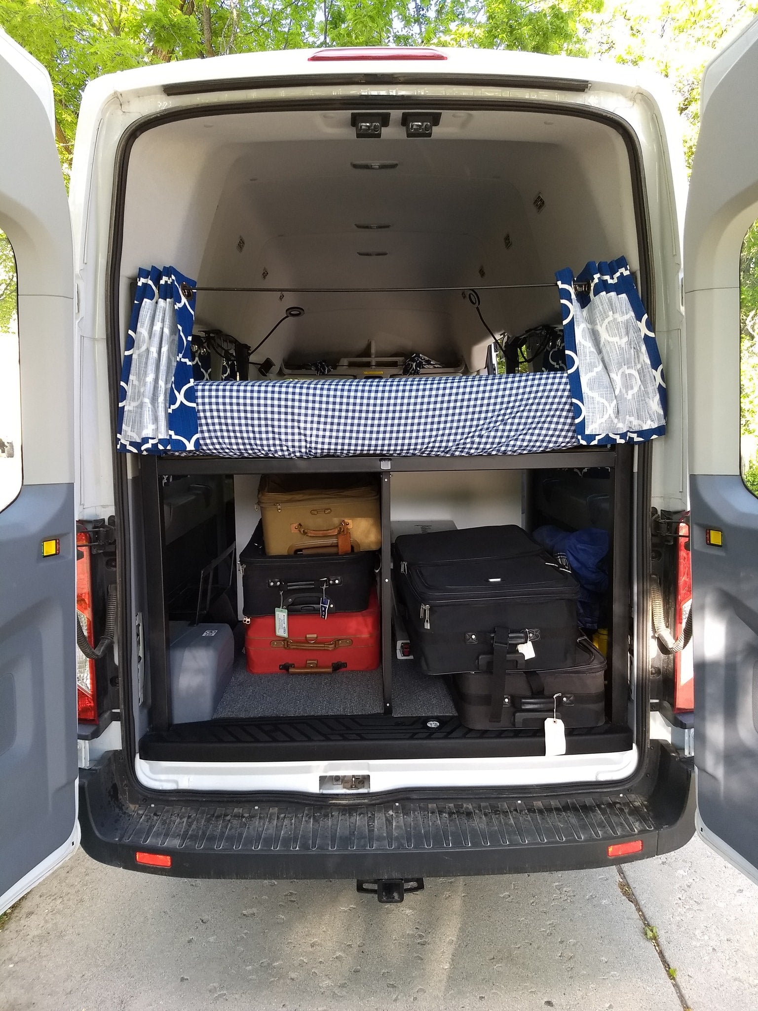 RV rental interior: Organized camper van with an elevated bed, curtains, and luggage storage below.