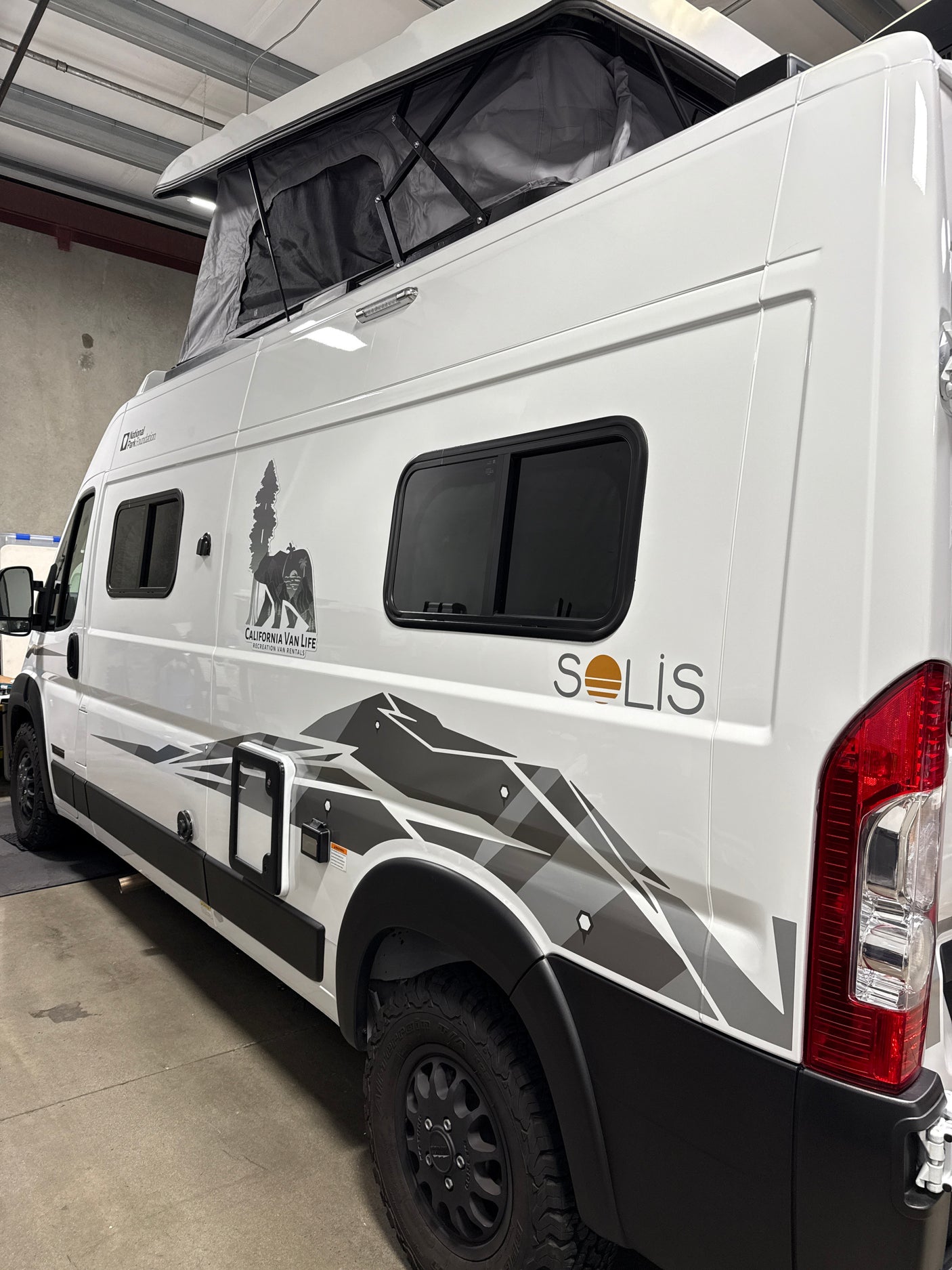 Side view of a white Solis camper van with pop-top roof and mountain graphics, perfect for your next RV rental.