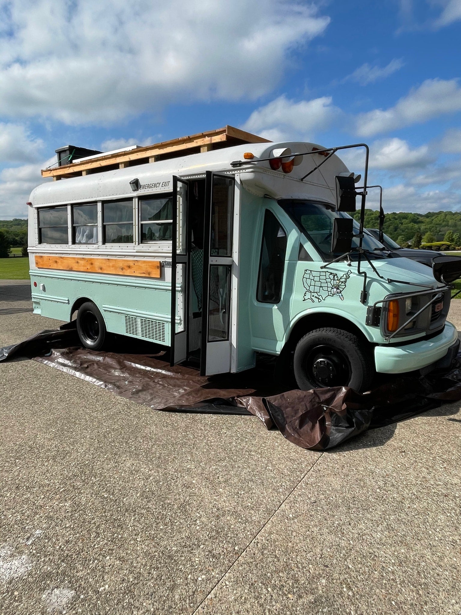 and tiled shower.|Skoolie RV rental against stunning Grand Teton mountains. Blue skies for an epic road trip adventure.|RV rental outdoor cooking: French press and pot on a Coleman propane stove next to a converted bus in a field.|Mint GMC skoolie with a man on the roof using binoculars in a sunny field