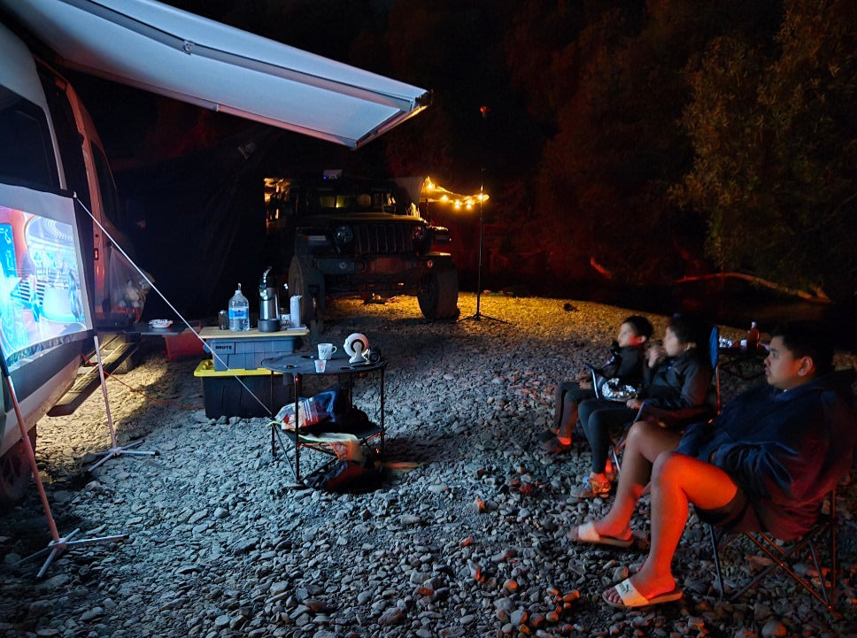 An RV rental transforms a rocky campsite into an outdoor cinema for a family night under the stars.