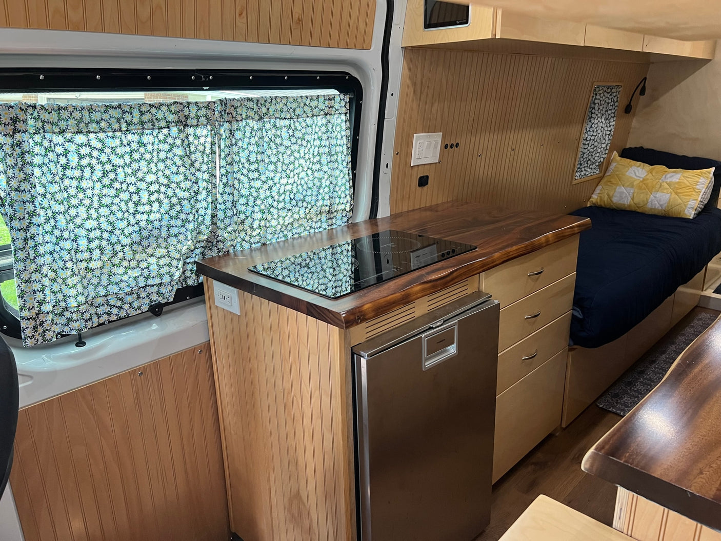 Spacious RV rental interior featuring a modern kitchenette, cozy bed, and custom wood finishes for comfortable travel.
