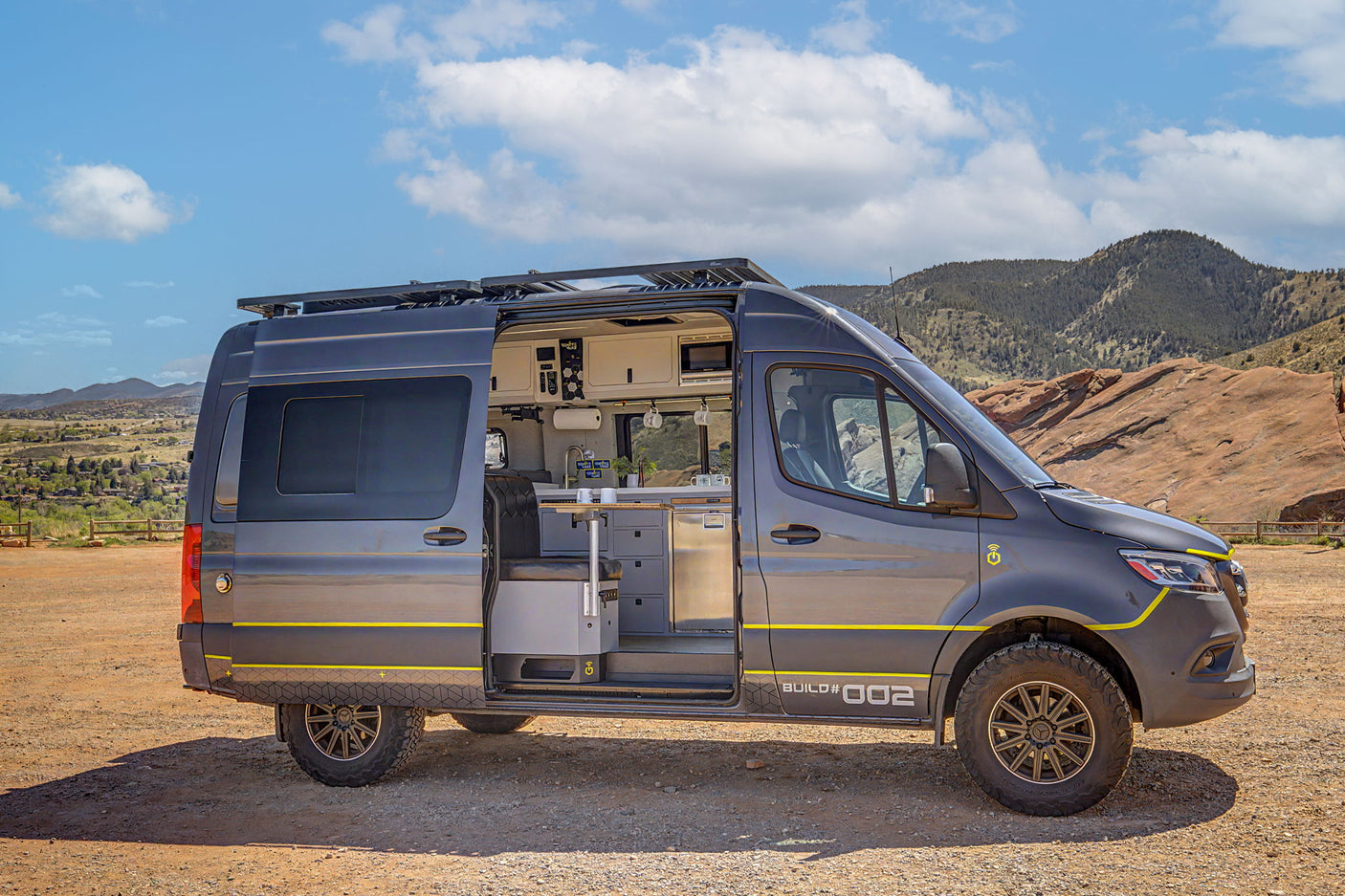 Custom gray camper van, open door reveals modern interior, parked off-road. Perfect RV rental for scenic mountain adventure.