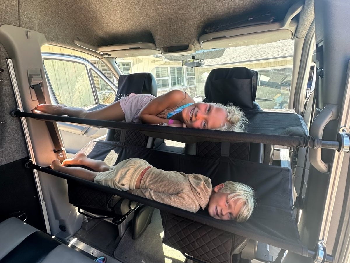 and detached seats.|View inside an RV rental camper van conversion. Features an elevated bed