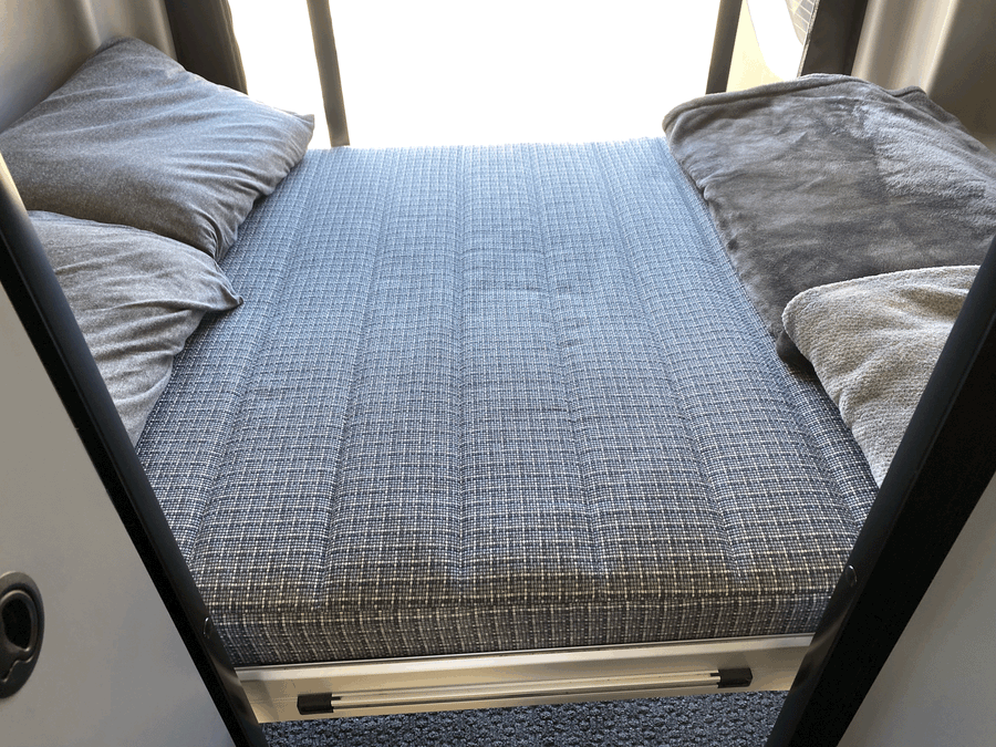 Cozy RV rental sleeping area featuring a patterned mattress, soft pillows, and blankets for comfortable travel.