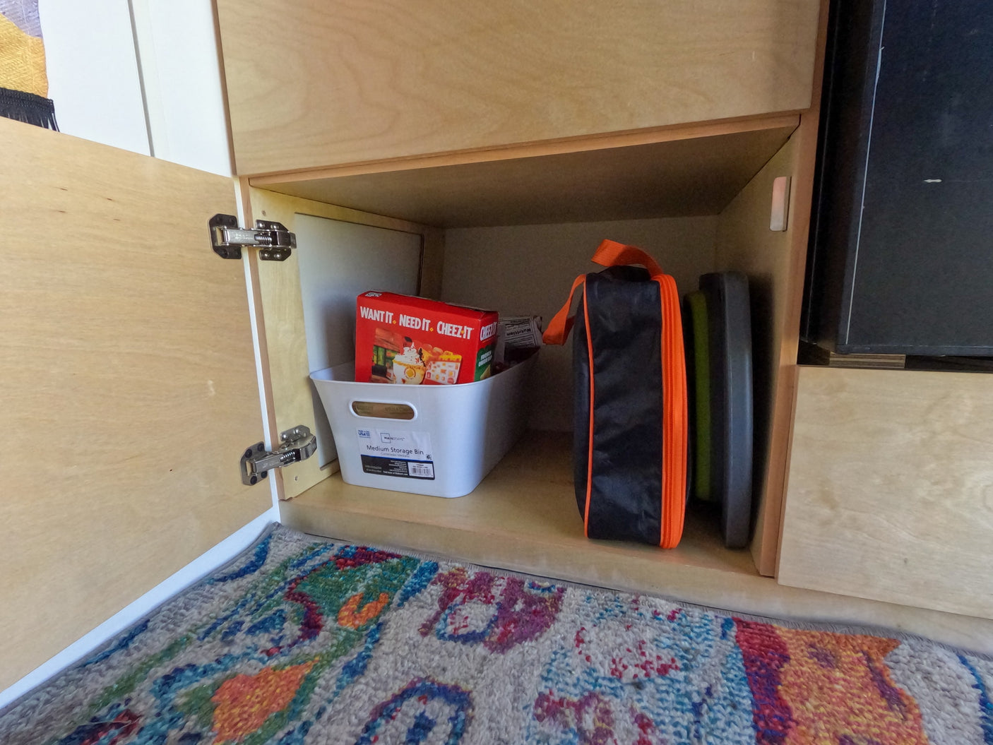Organized RV rental cabinet with Cheez-It snacks in a storage bin and a travel bag, ideal for compact living.