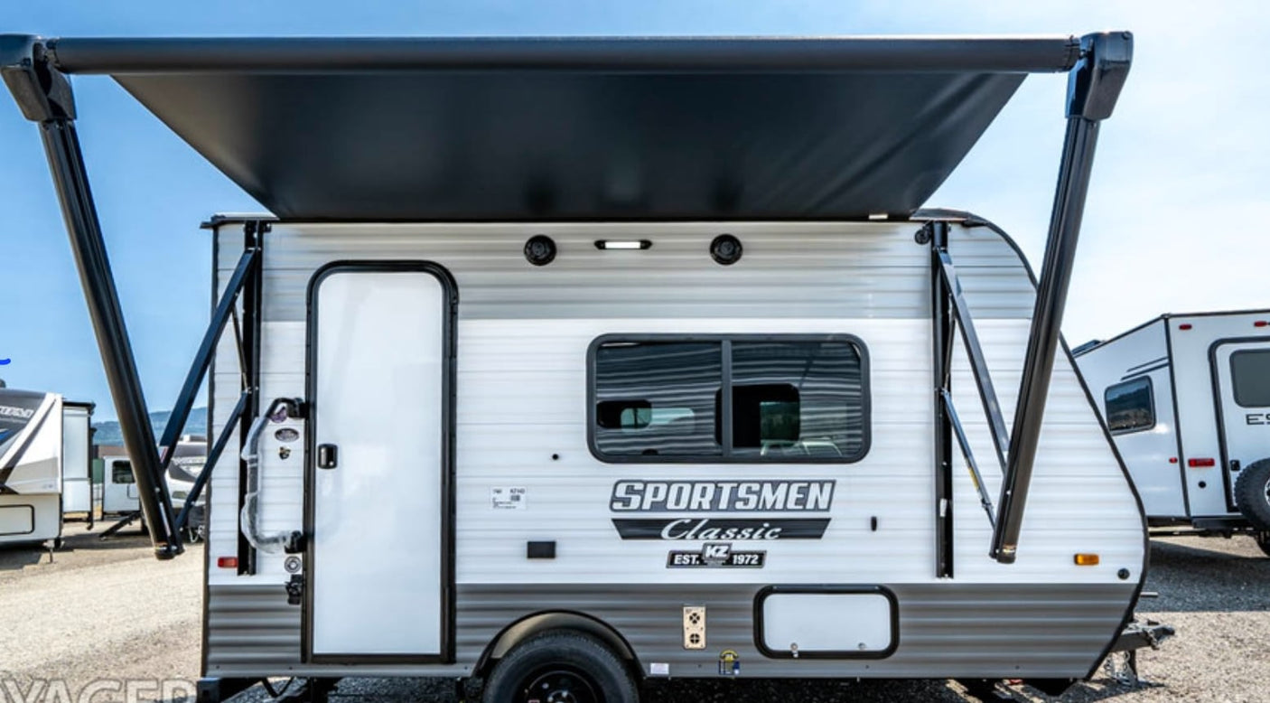 A white and gray Sportsmen Classic travel trailer with a large black extended awning, perfect for an rv rental.