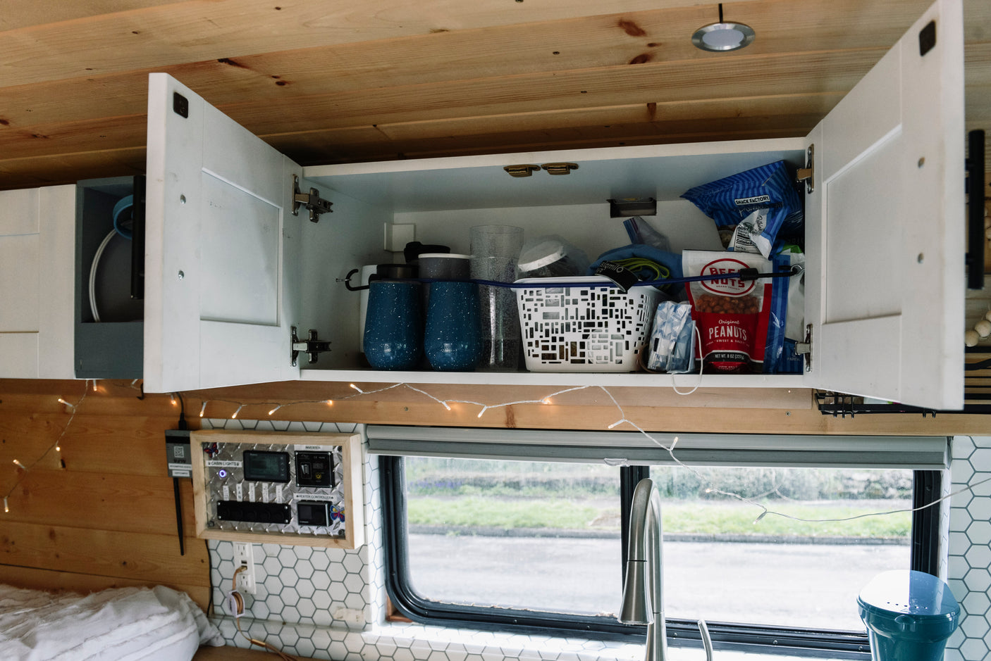 RV rental interior: open cabinet with snacks & cups, control panel, and decorative string lights for cozy mobile living.