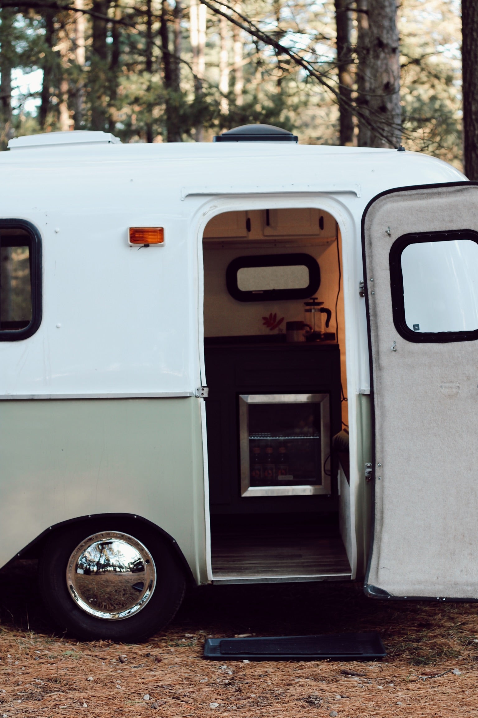 Cozy RV rental in the forest with an open door showing the interior kitchenette. Perfect for glamping.