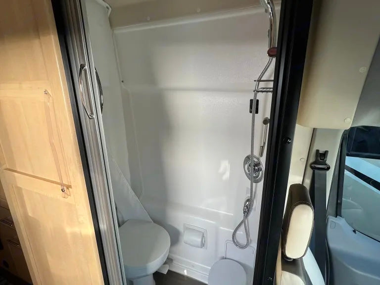 This RV rental features a compact camper bathroom with a clean white shower and toilet, perfect for your motorhome adventure.