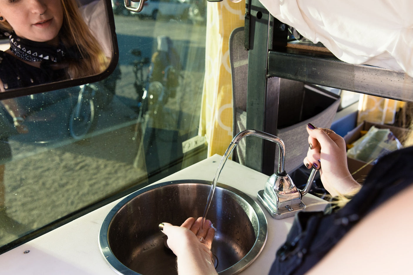 Washing hands in a compact RV rental sink with a pump faucet. User's reflection seen in the window.