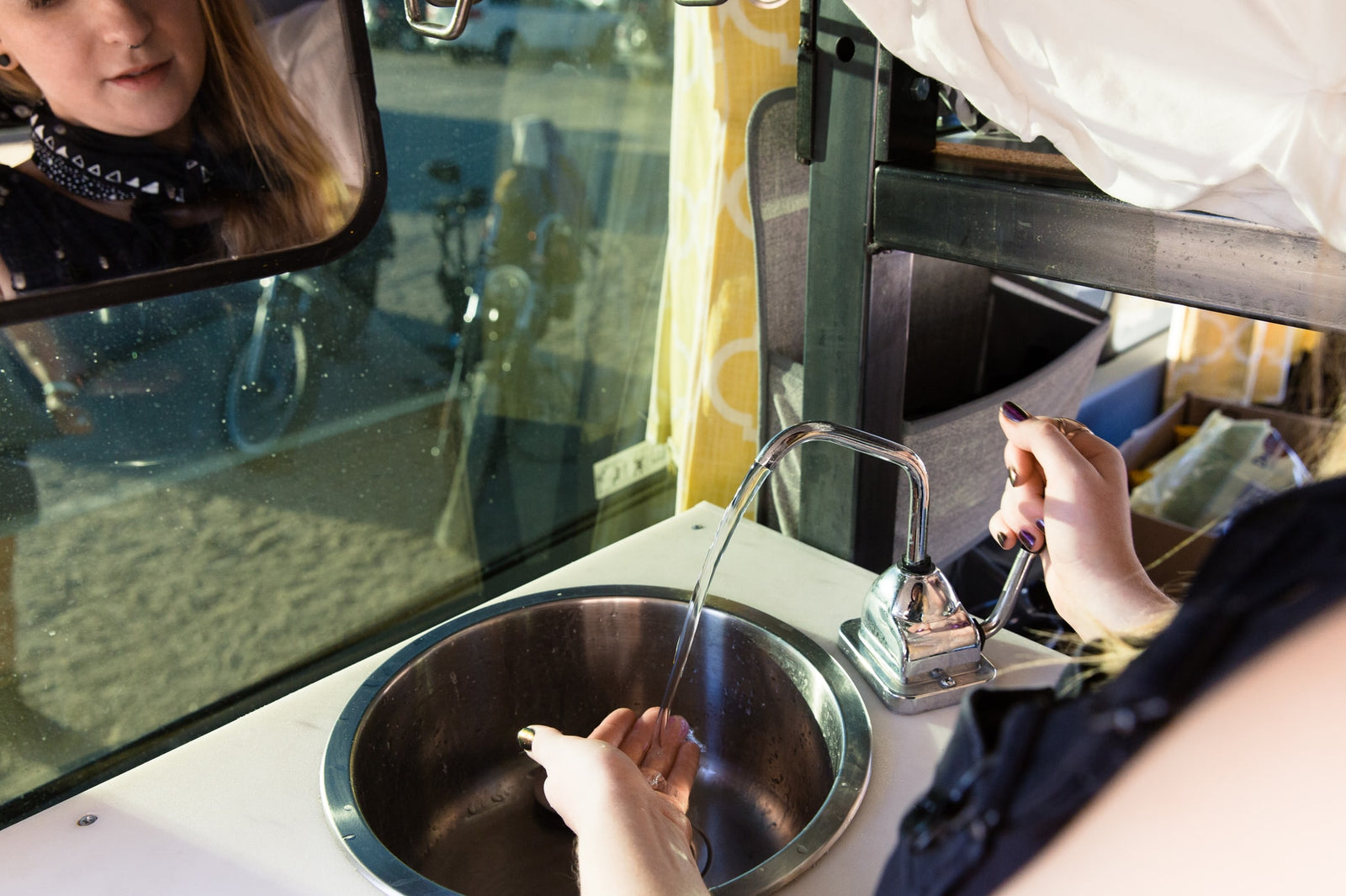 Washing hands in a compact RV rental sink with a pump faucet. User's reflection seen in the window.
