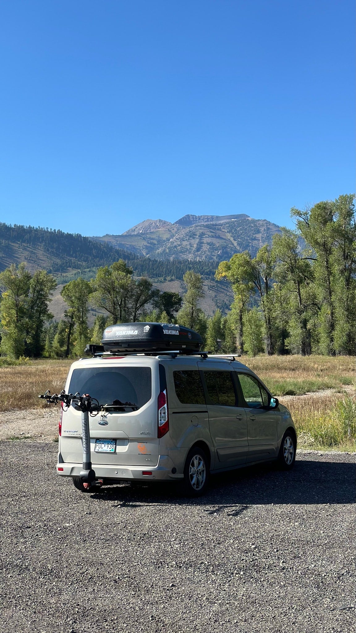 This RV rental van, equipped with a cargo box & scooter, is parked with mountains & trees in the background. — photo 2