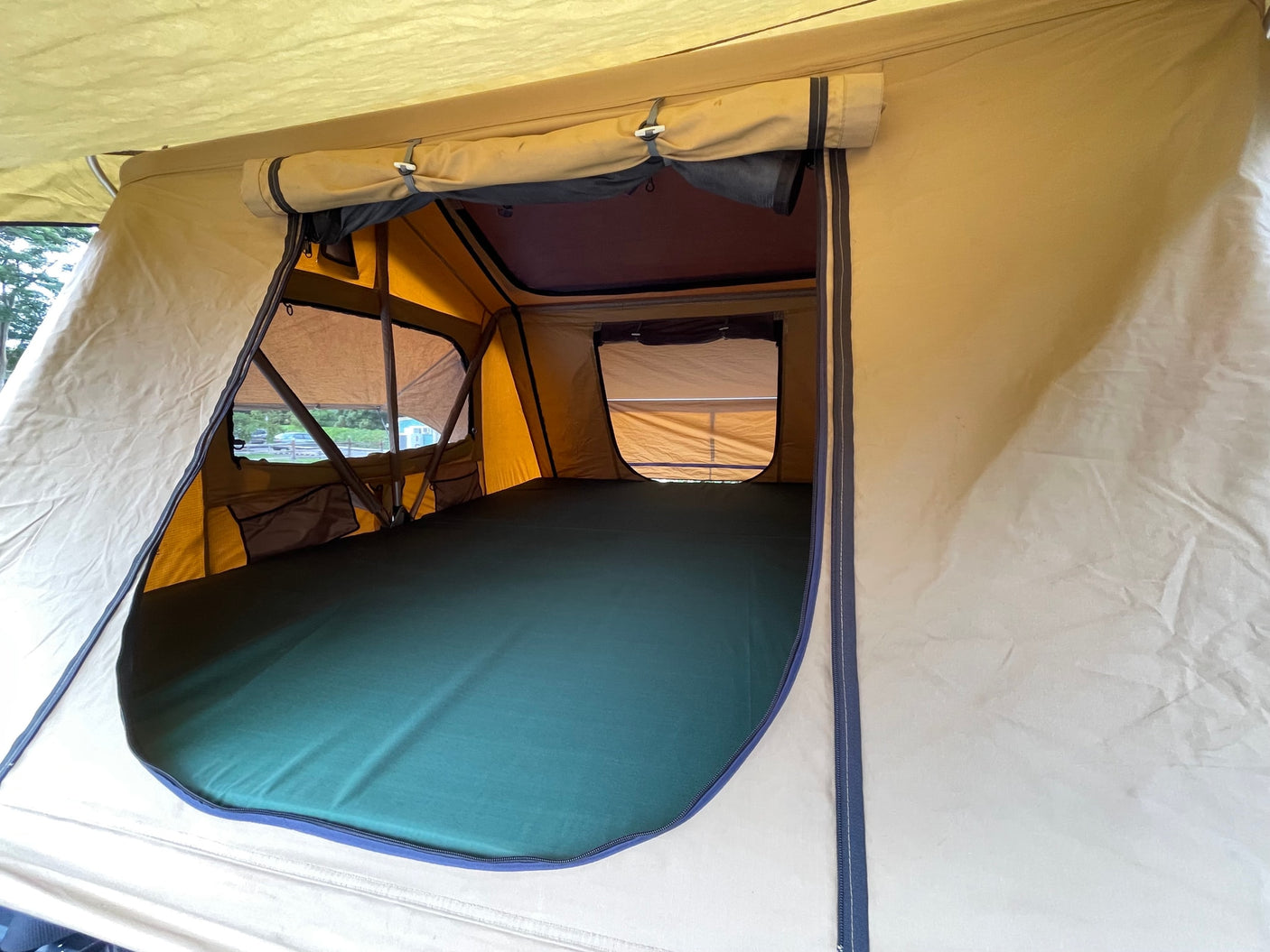 Inside a spacious rooftop tent with a dark green mattress, mesh windows, and roll-up blinds, ideal for your next RV rental adventure.