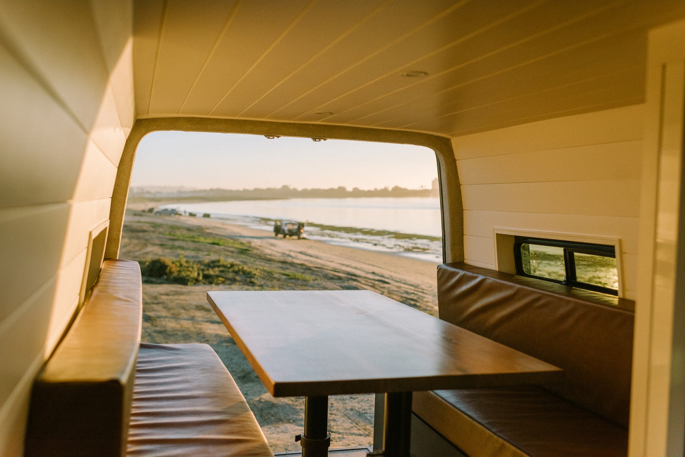 Warm light fills this RV rental's dining area & leather benches, overlooking a serene beach with a parked vehicle. — photo 32