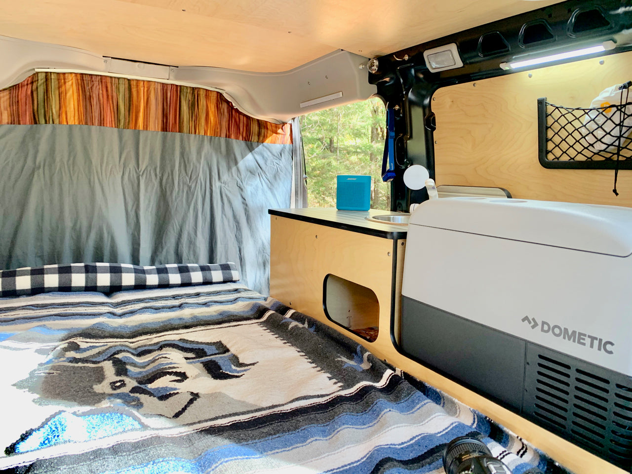 RV rental interior: cozy bed, compact kitchen with sink & Dometic cooler, ready for adventures.