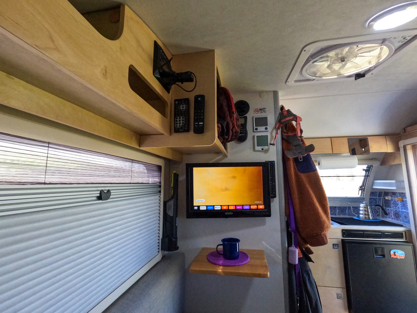 Compact rv rental interior with TV, kitchen, blinds, and overhead storage, maximizing comfort for travel.
