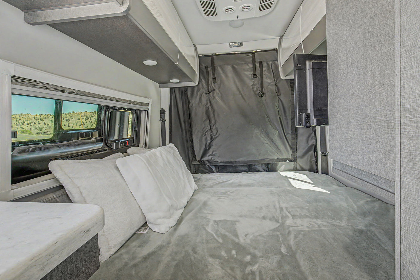 Inside a modern RV rental: a plush bed, scenic window view, and TV offer comfort on the road.