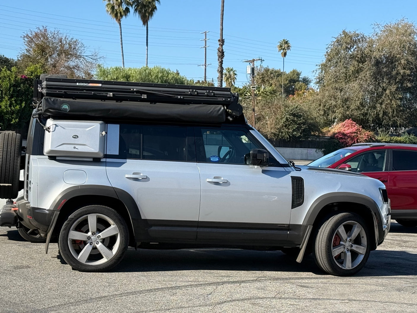 A silver Land Rover Defender with a Roofnest rooftop tent and side gear box, perfect for an adventure RV rental.