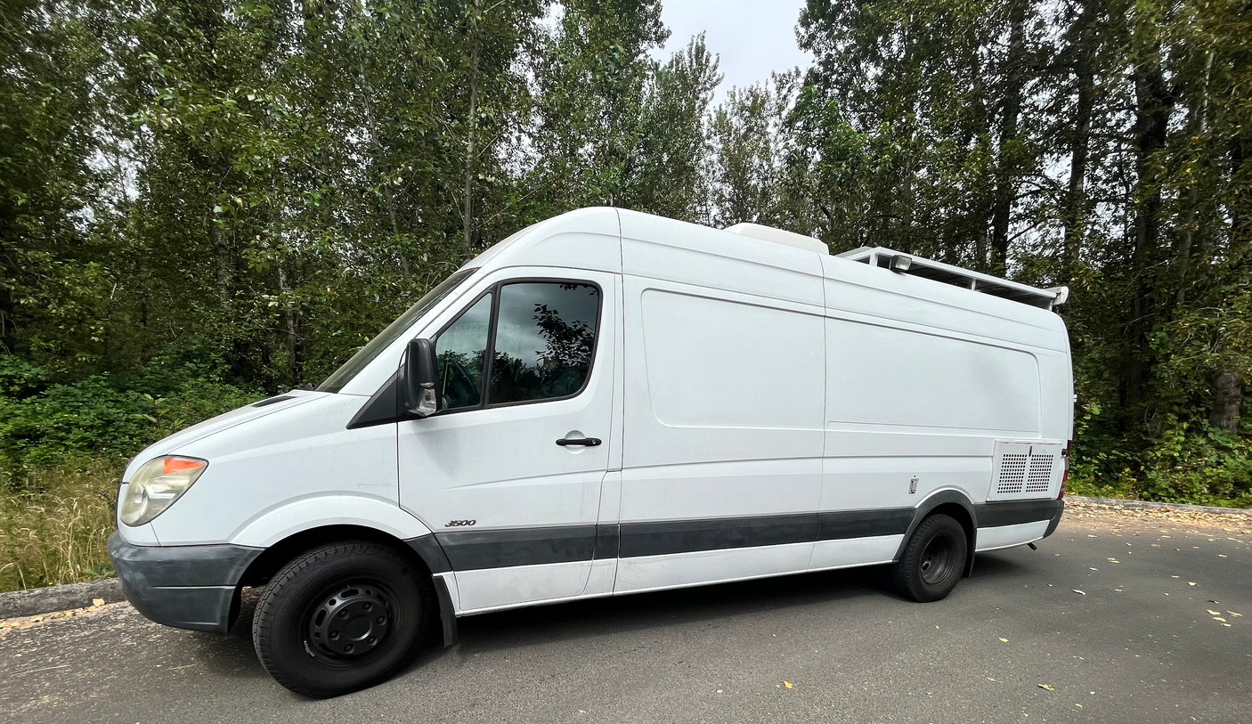 This white Mercedes Sprinter 3500 van, ideal for RV rental, is perfect for a road trip adventure. Parked by trees.