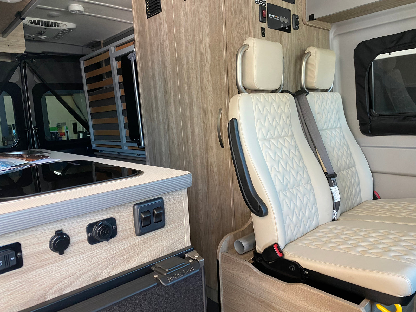 Inside a functional RV rental: discover the compact kitchen, comfortable quilted seating, and wall-mounted solar controls.