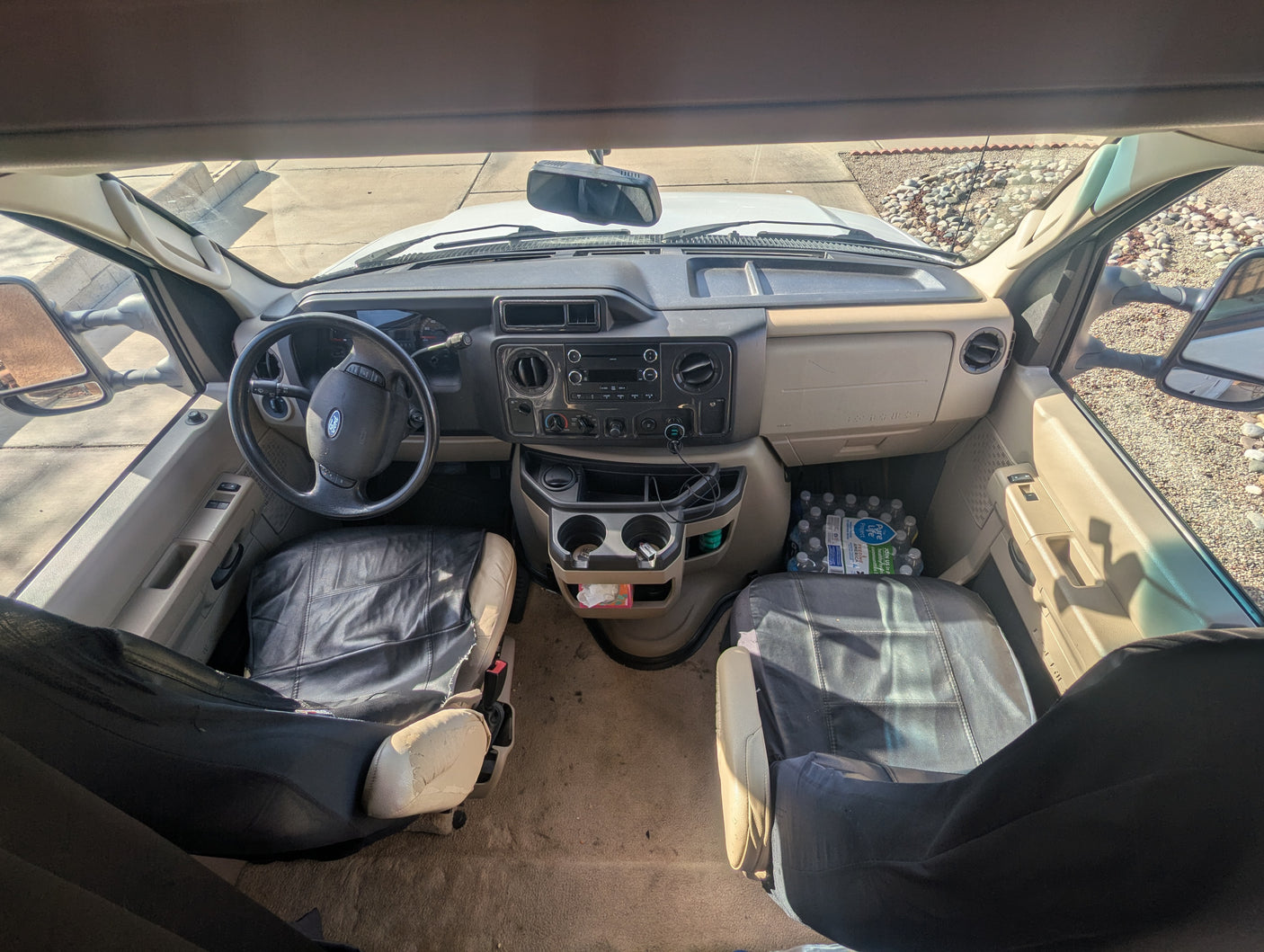 RV rental interior cabin view showing driver and passenger seats, dashboard with steering wheel, cup holders, and bottled water.