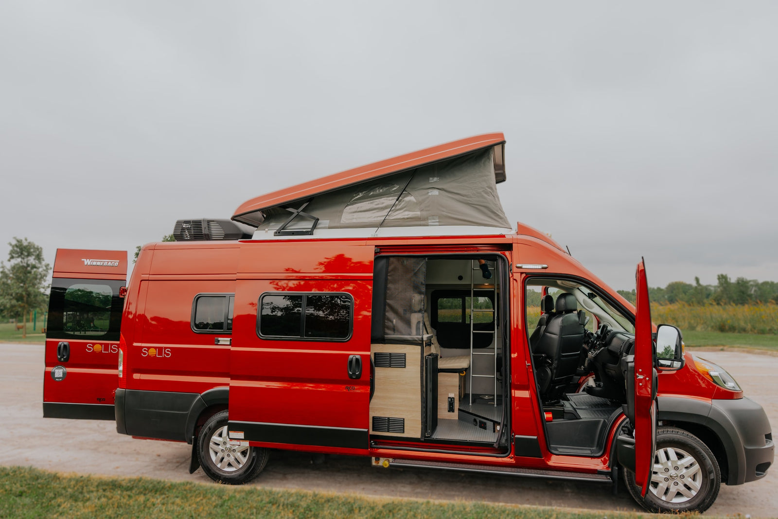 Vibrant red Winnebago Solis camper van with an open pop-top and interior visible, perfect for an RV rental.