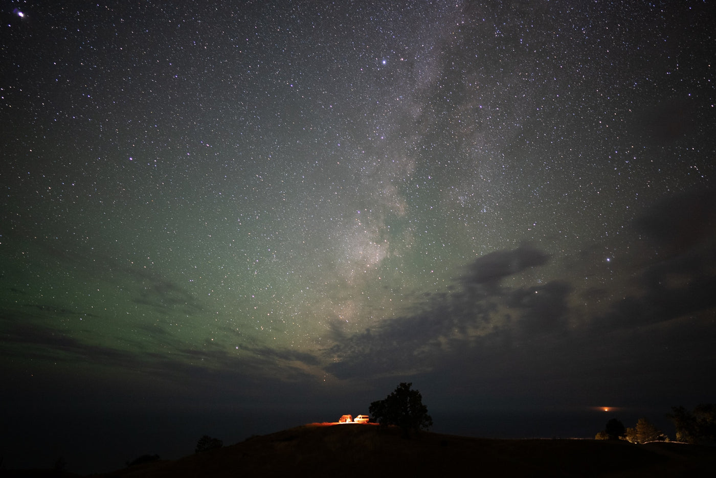 Milky Way and green airglow illuminate an RV rental, car, and tree on a hill, creating a stunning starry night camp scene. — photo 7