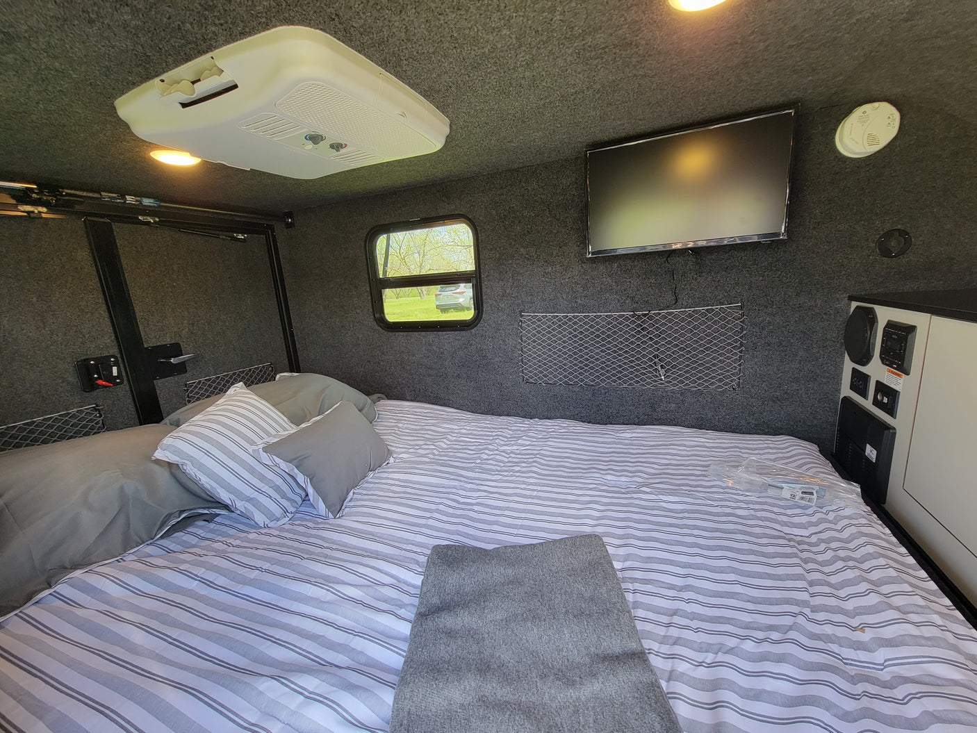 Cozy RV rental interior with a spacious bed, mounted TV, AC unit, and window views.