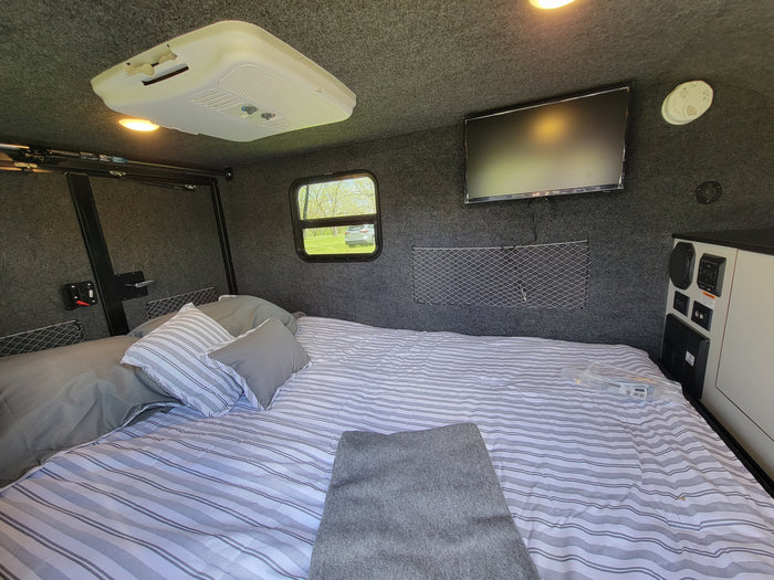 Cozy RV rental interior with a spacious bed, mounted TV, AC unit, and window views.